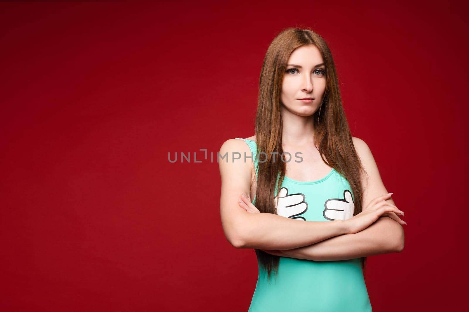 Studio portrait of unsatisfied young brunette caucasian woman with wavy hair in overall with colorful pattern holding arms folded and looking at camera with grief, dissatisfaction, anger and disbelief. Isolate.