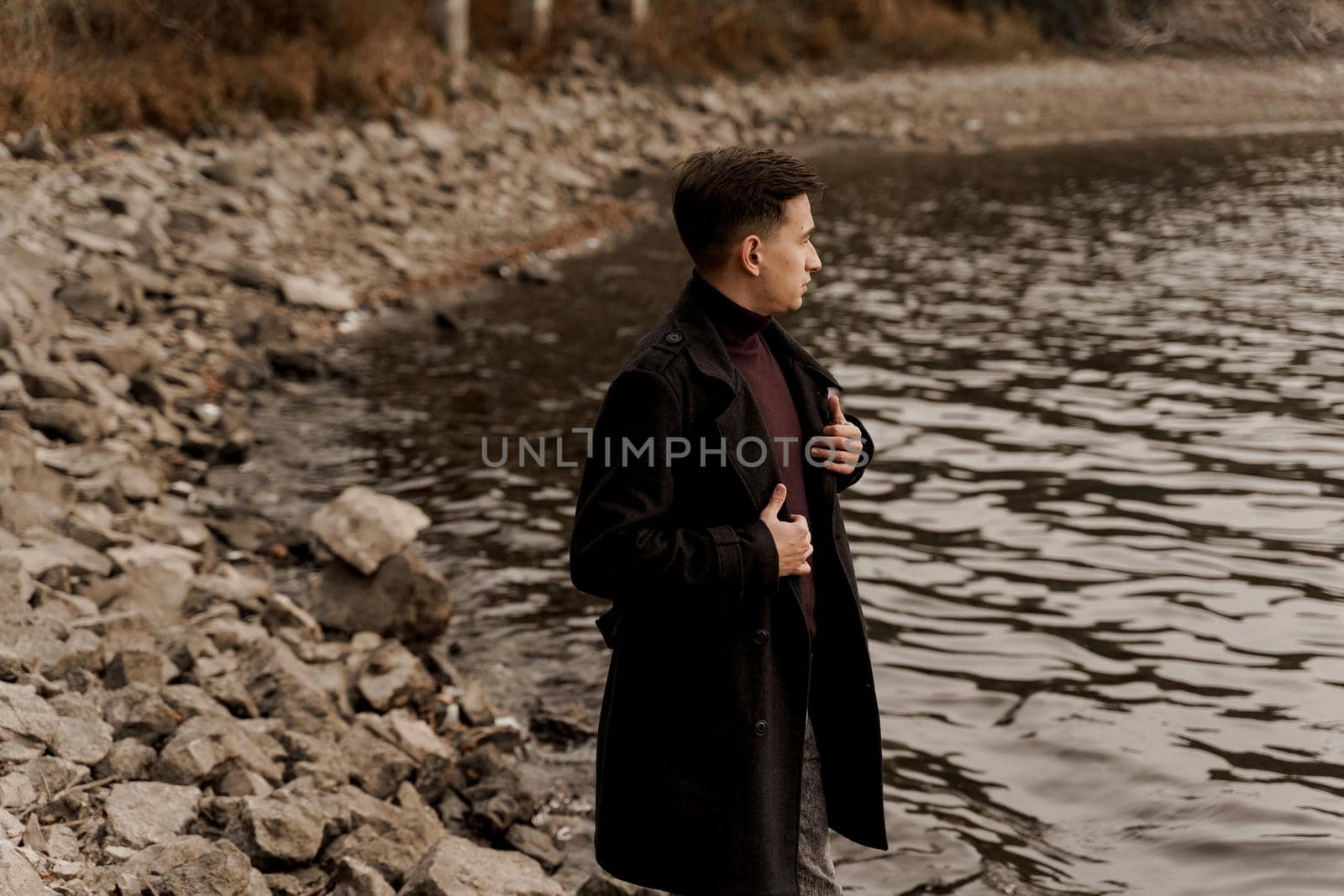 Confident business man walks near lake and thinks about his business during quarantine coronavirus covid-19 period. Handsome male weared formal black coat. by Rabizo