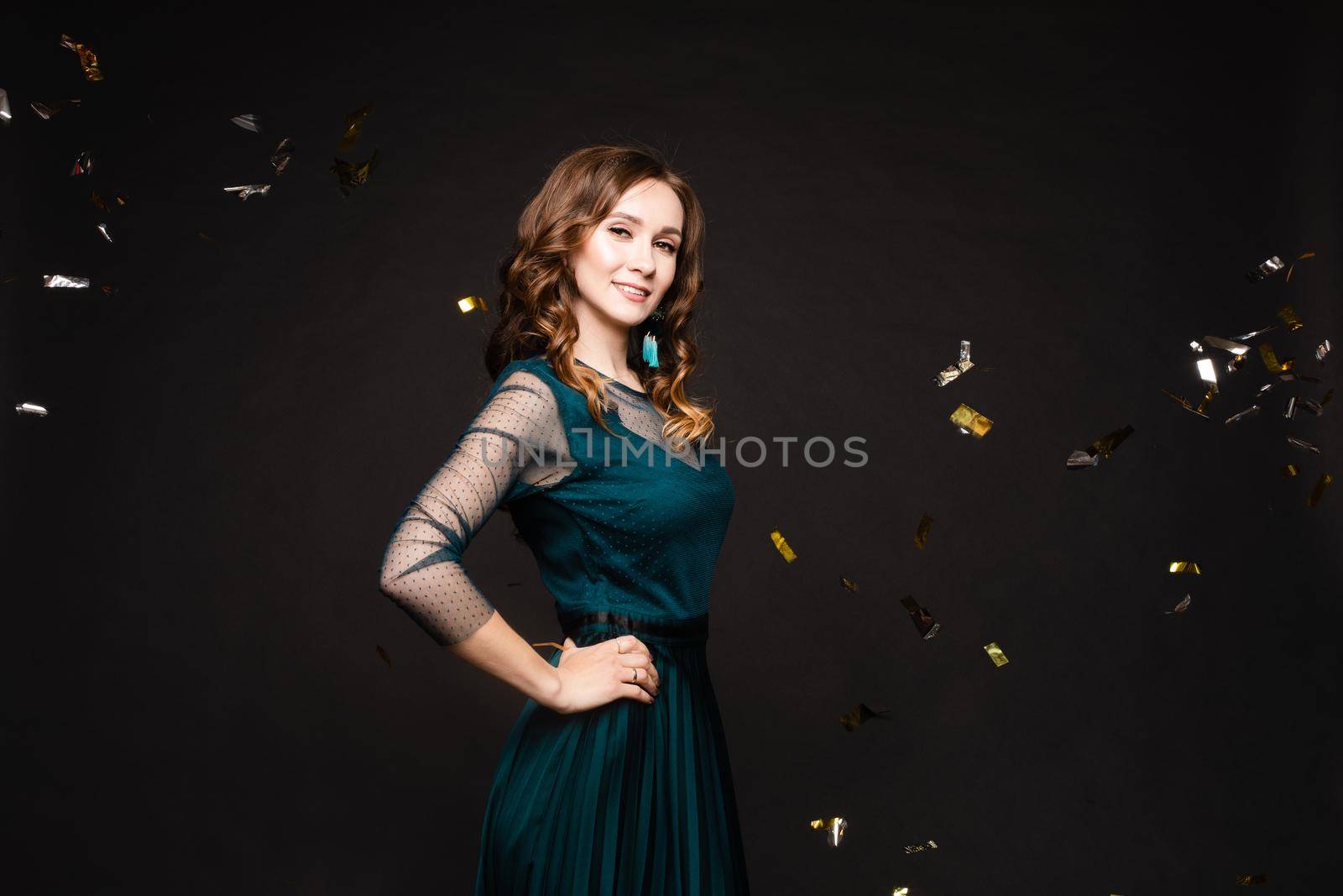 Front view of elegant woman wearing long black dress looking at camera and smiling on black isolated background. Attractive blonde with long legs posing in studio. Concept of party and beauty.