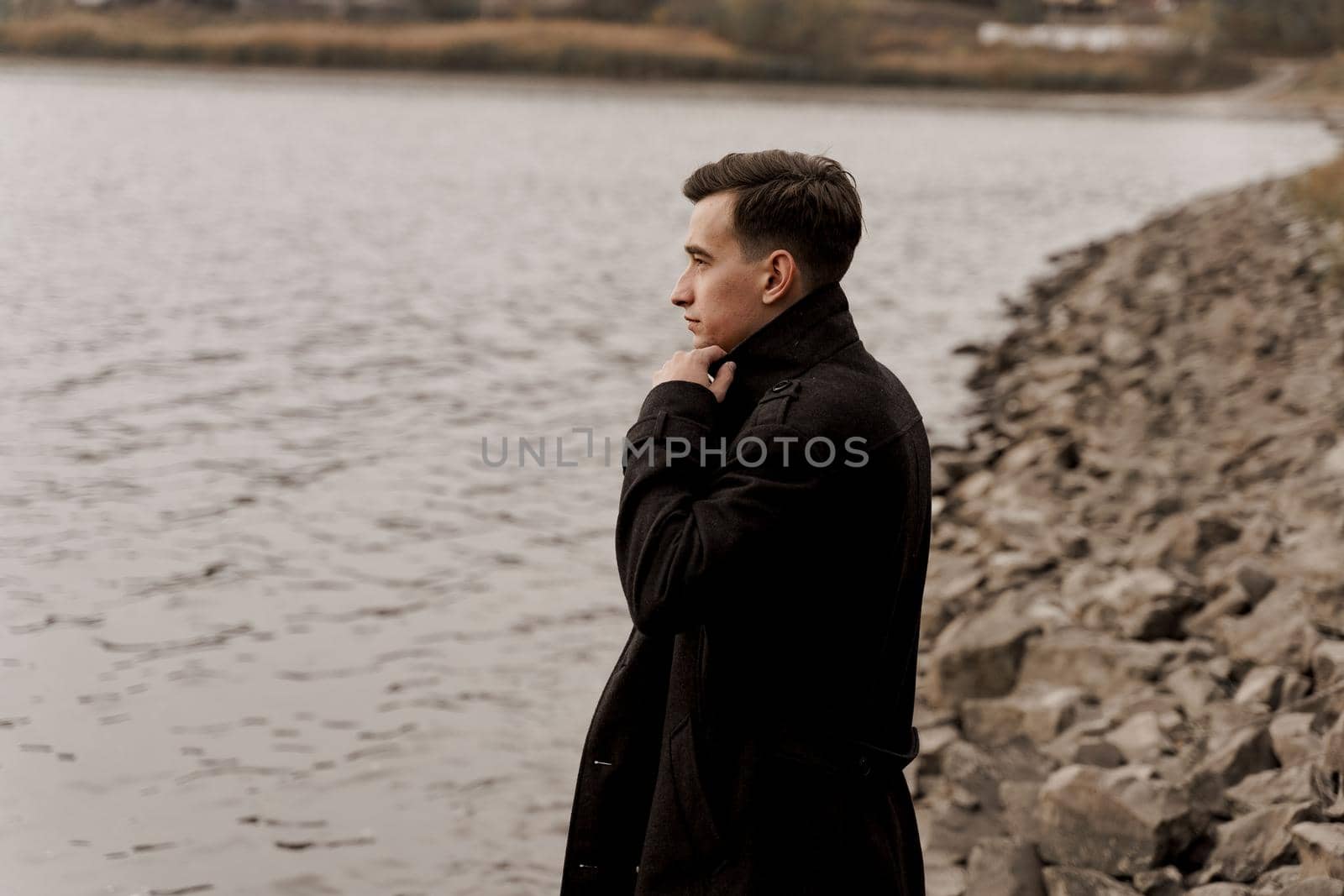 Confident male model weared black fashion coat. Handsome man walks near lake. by Rabizo