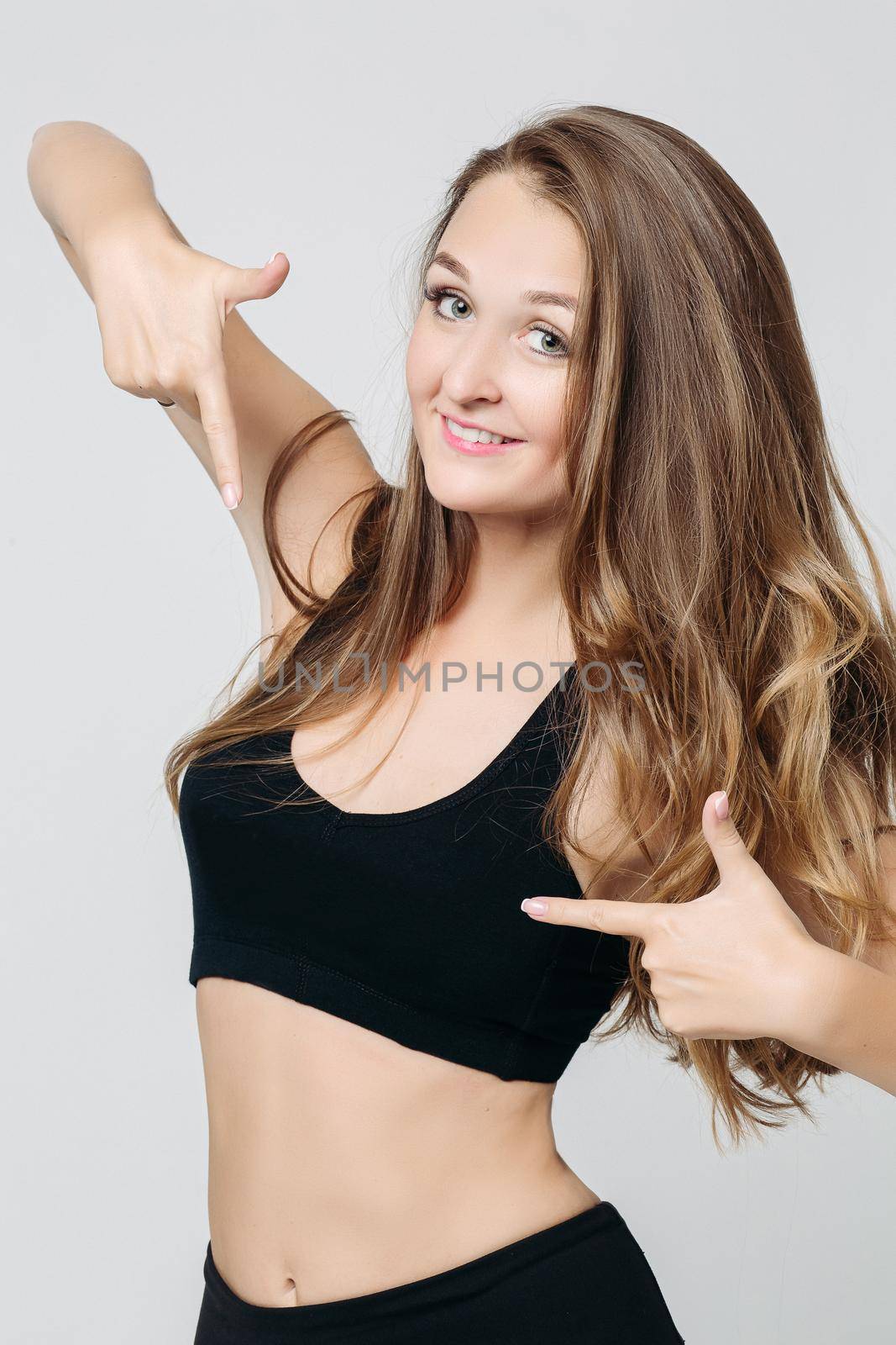 Smiling and beautiful woman in black sports wear gesturing by two hands on her top. Positivity girl pointing by finger at herself. Concept of sport fasion and shopping sale.