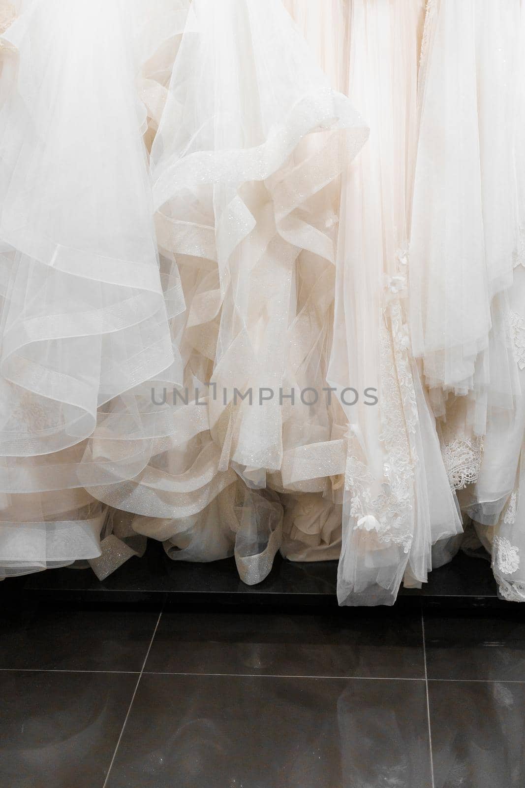 Cloth of wedding dresses made of silk chiffon, tulle, lace. Vertical photo for social networks. Beautiful White cream bridal dress on hangers in wedding salon. Pearls, crystals pendants on the sleeves