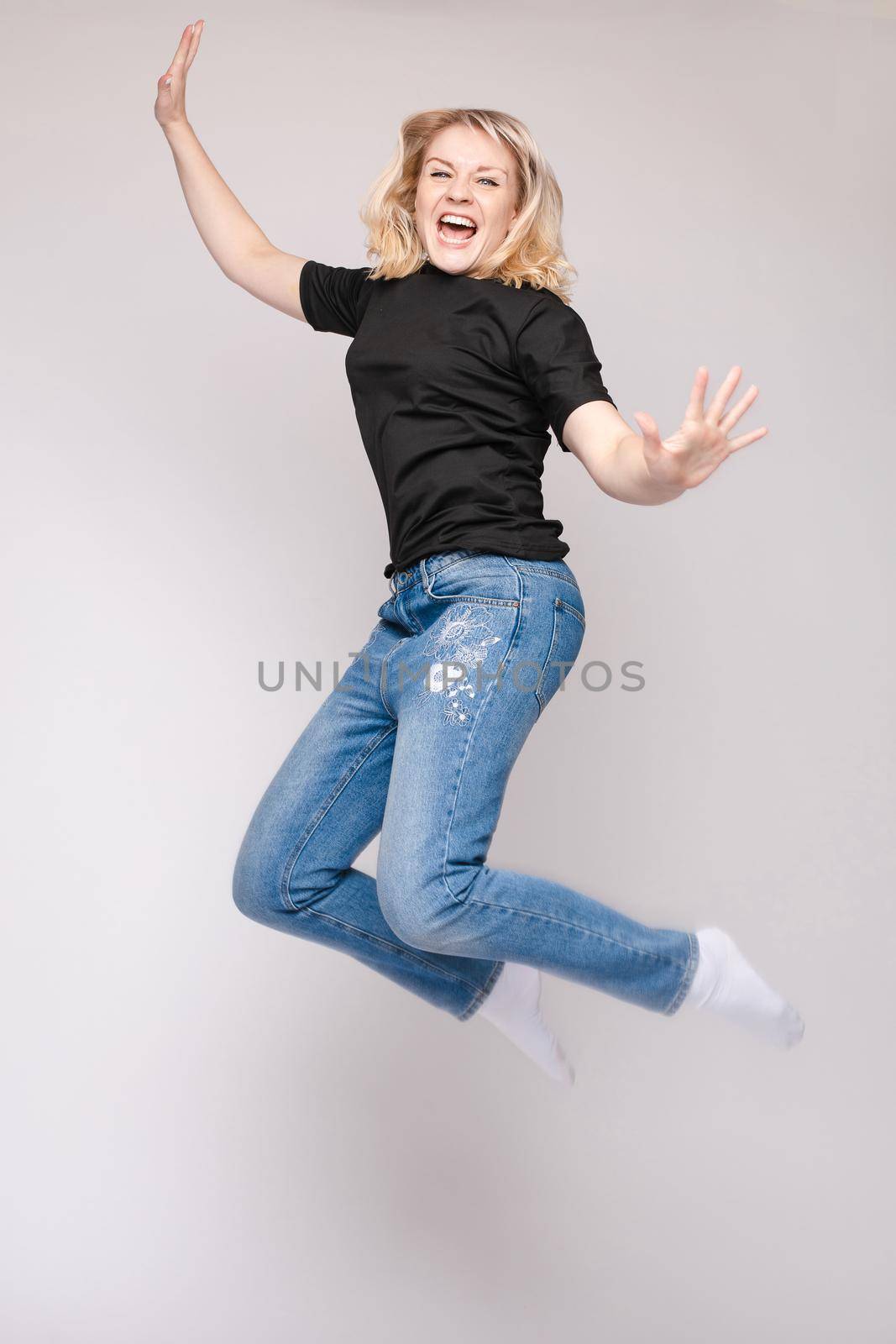 Full length isolate portrait of positive brunette young girl in jeans and t-shirt and sneakers jumping over yellow background. She is smiling at camera.