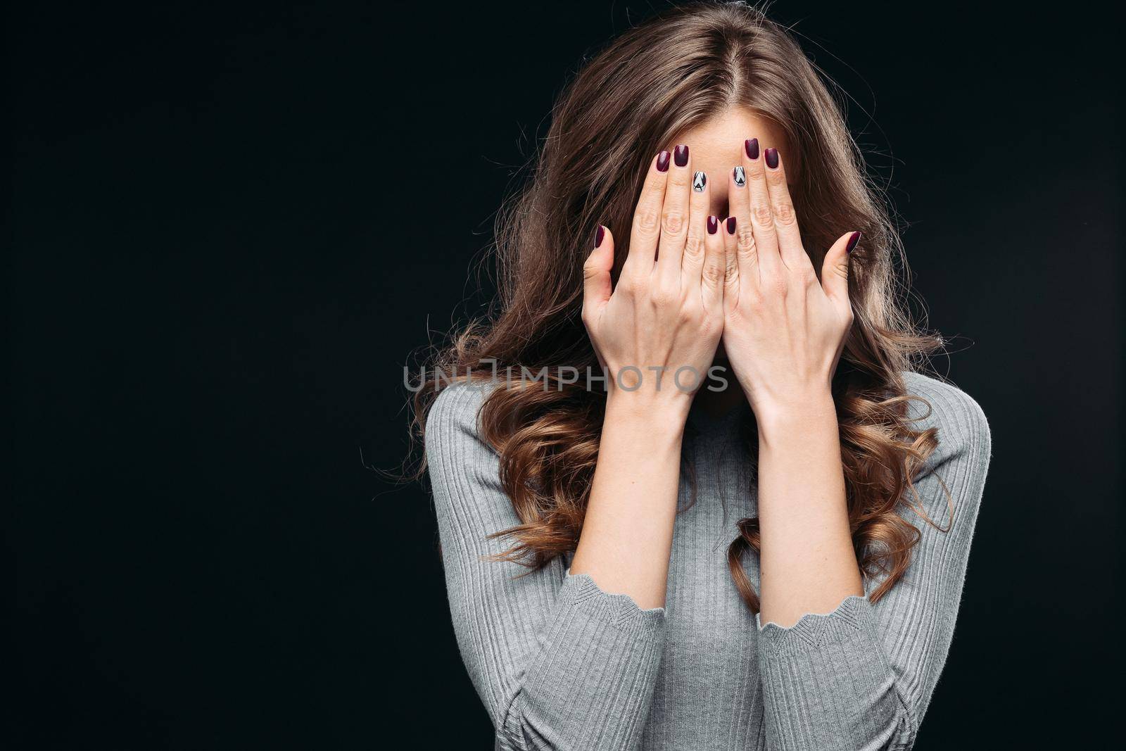 Waist up portrait of surprised beautiful girl with nice long hair, perfect makeup and fashion manicure. She is looking at camera with astonishment. Isolated on dark background