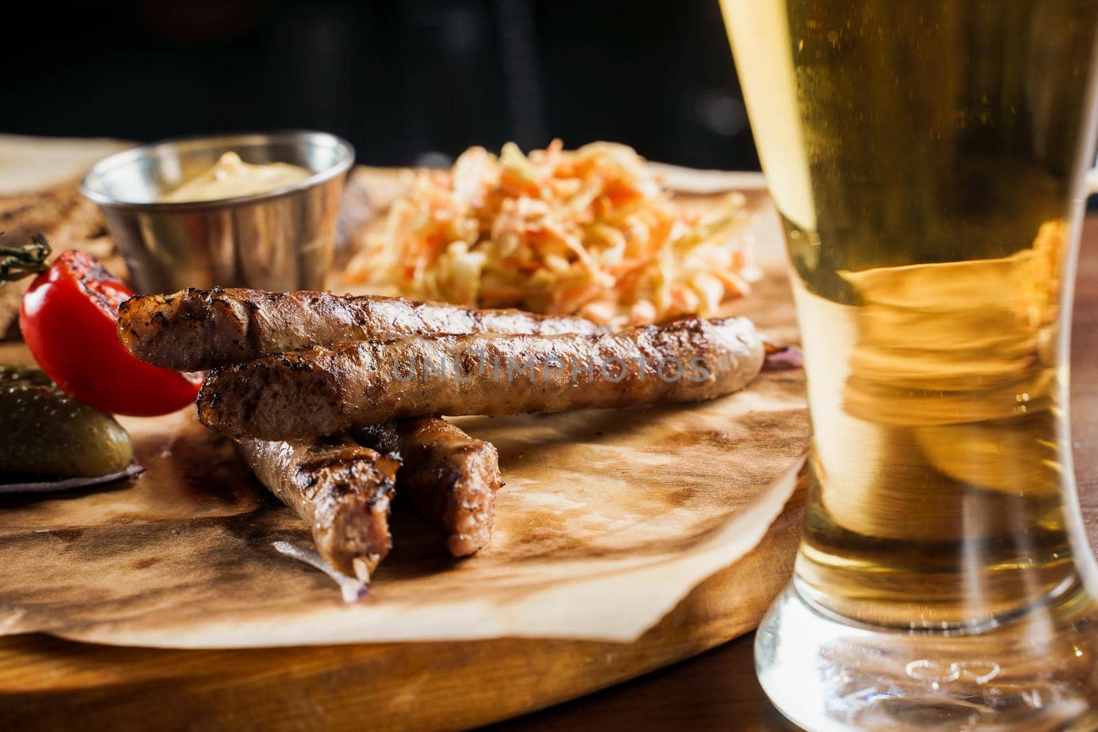 Grilled sausages with beer and vegetables with pickled cucumber, cabbage salad sauce and bread on parchment, top view.