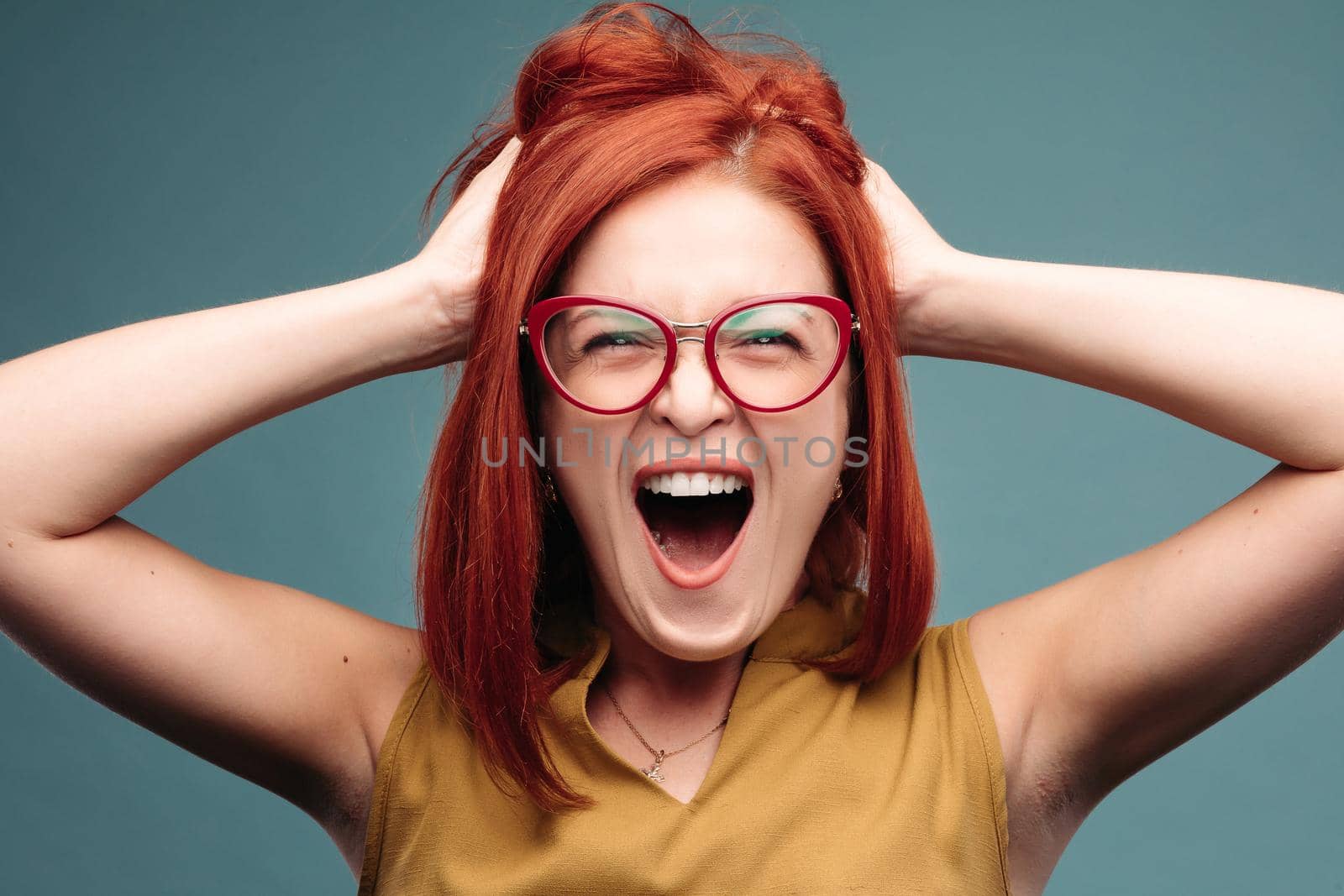 Front view of happy and positivity red haired woman in eyeglasses shouting holding head by hands, looking at camera. Emotionally girl smiling and surprised, having good shock. Drive and happy concept.