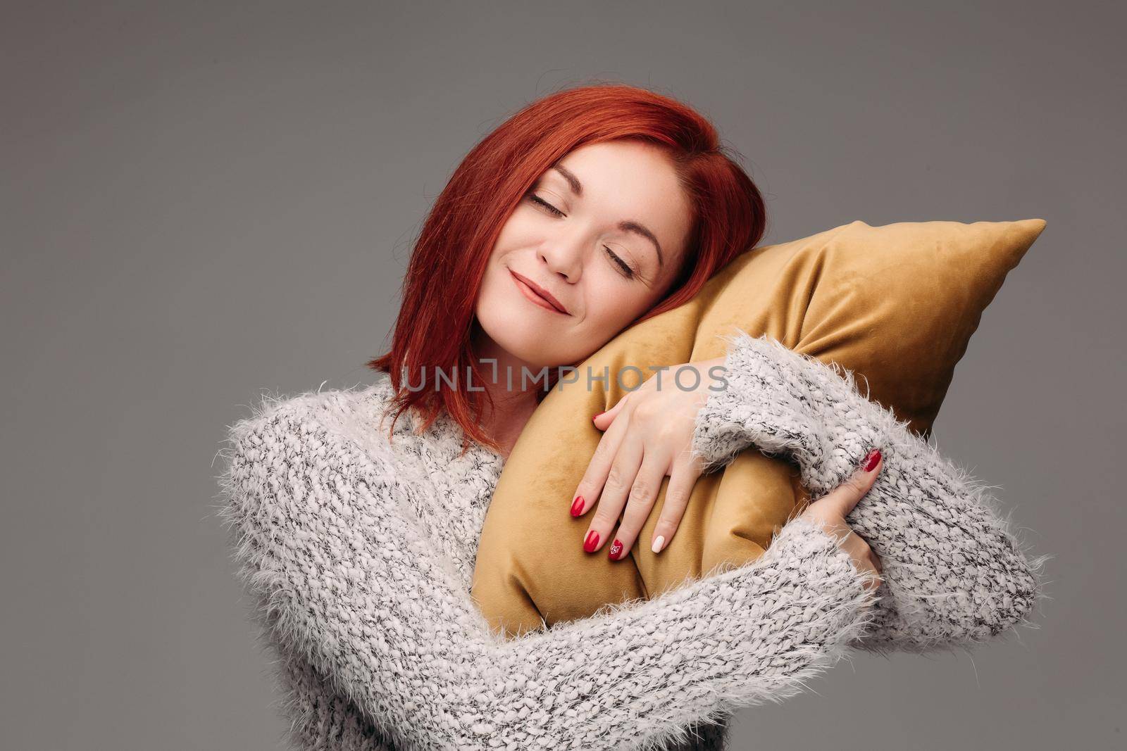 Studio portrait of a woman in a sweater hugging a pillow. The concept of fatigue or odicancy. Isolated on a gray background.