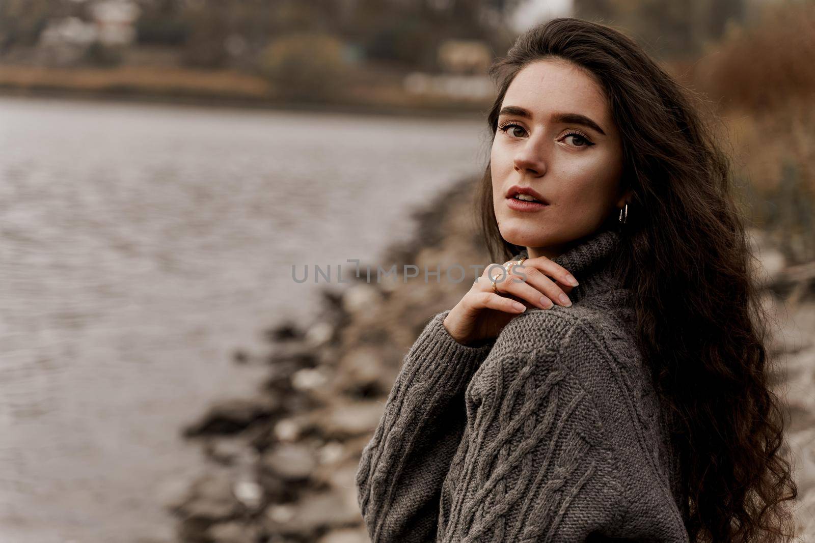 Girl with curly hair on the background of birch with stones and lake in autumn.