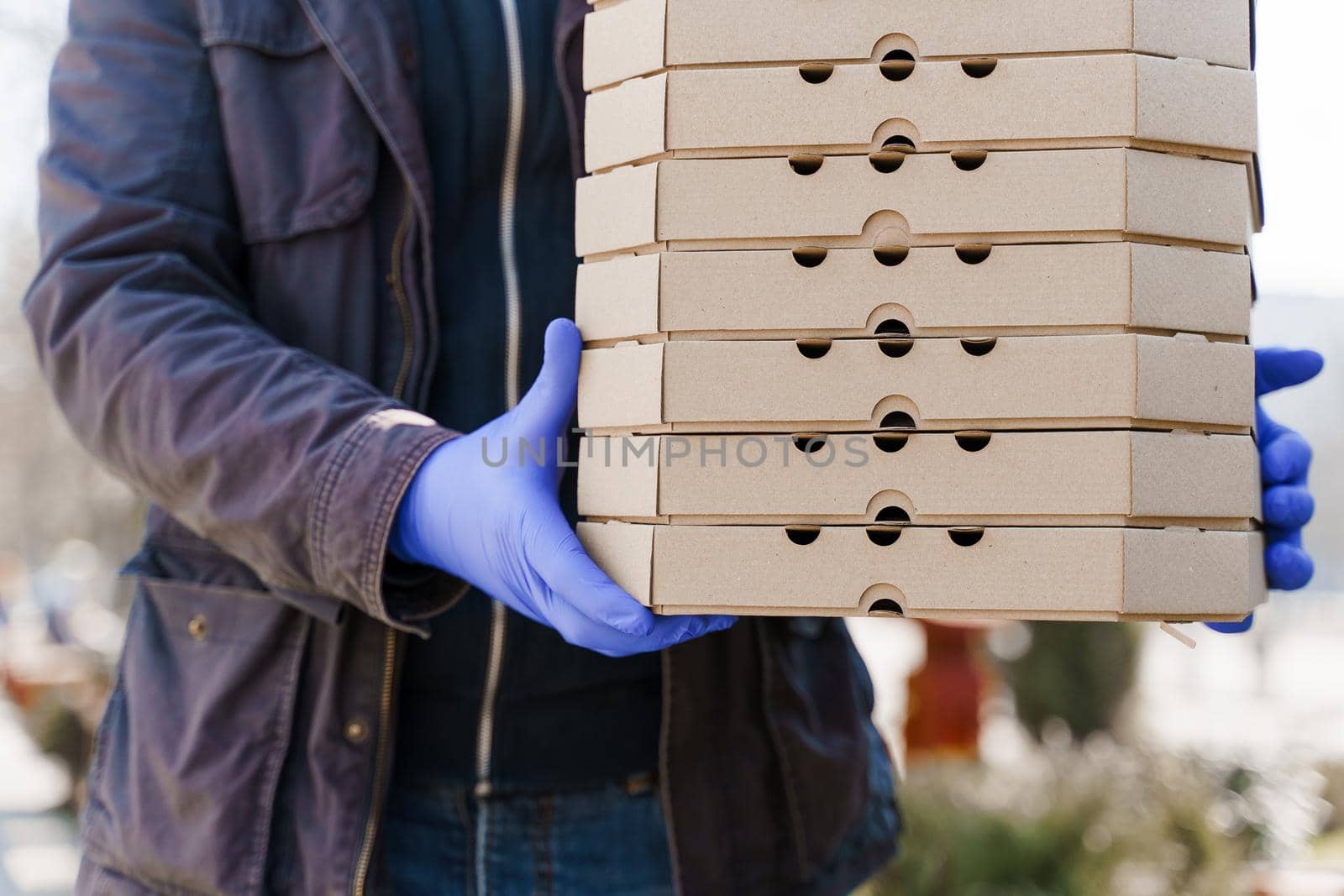 Food delivery courier in medical gloves with many boxes of pizza. Stay at home because coronavirus covid 19 killing people. Take away food by Rabizo