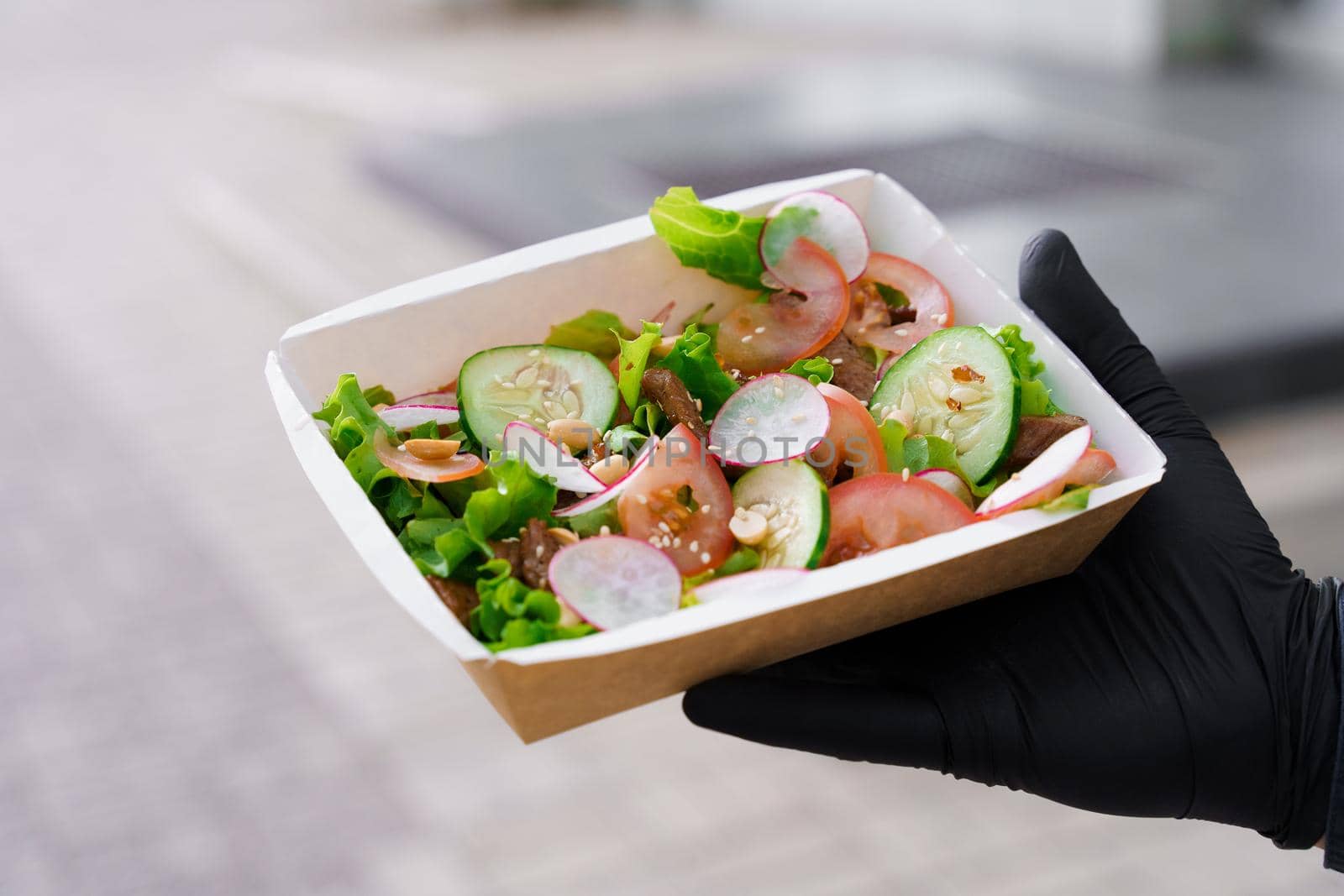 Green salad with veal and vagatables. Safety delivery with mask and black medical gloves at quarantine. Salad in eco thermo box.