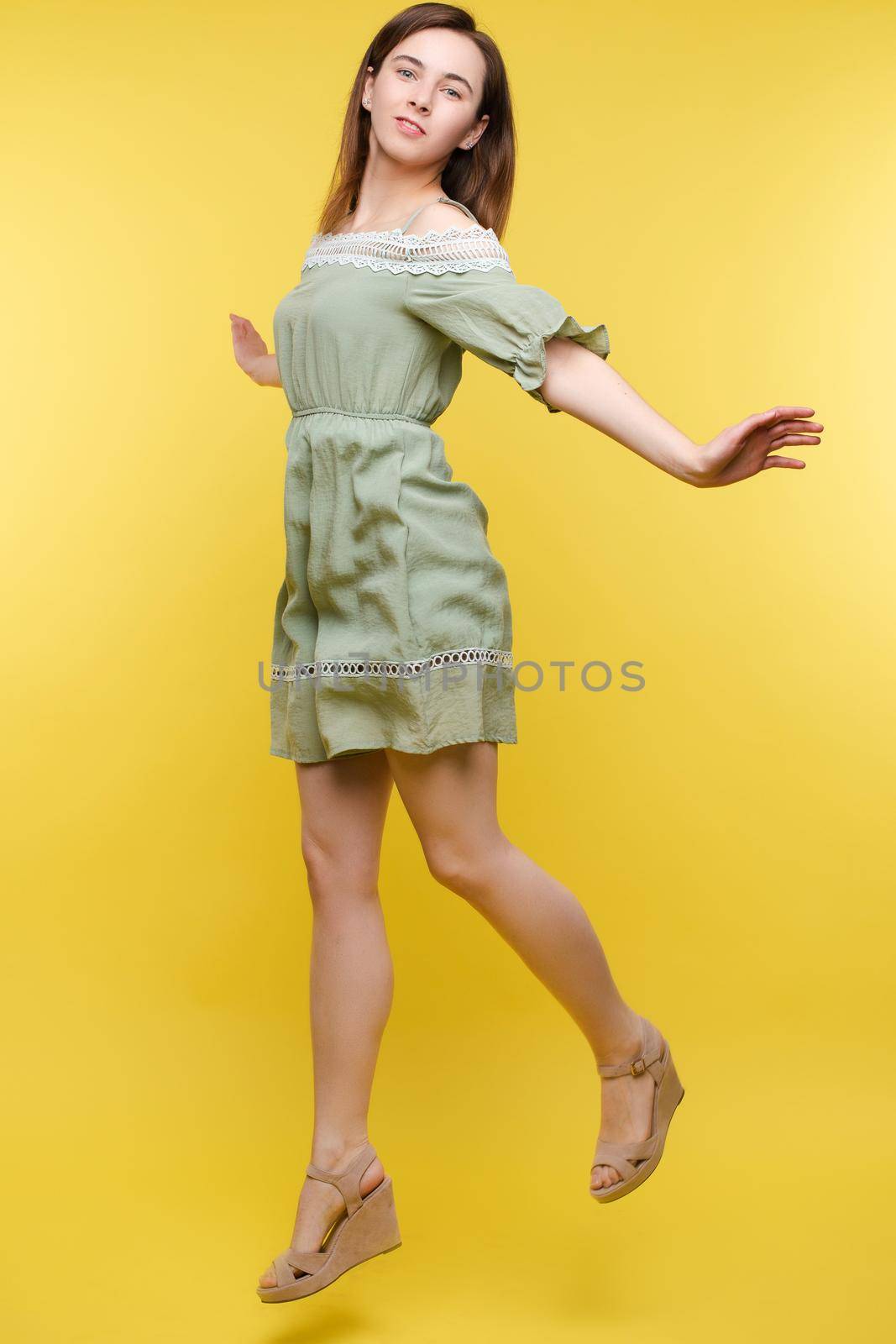 Full length isolate portrait of positive brunette young girl in jeans and t-shirt and sneakers jumping over yellow background. She is smiling at camera.