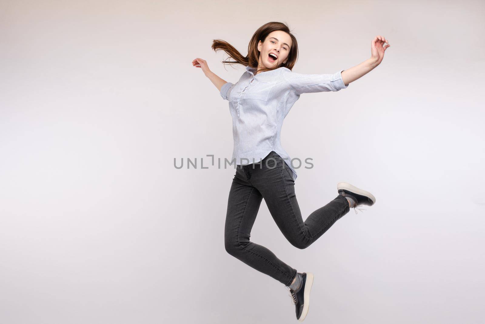 Cheerful brunette young woman in casual outlook jumping in mid air in studio. by StudioLucky