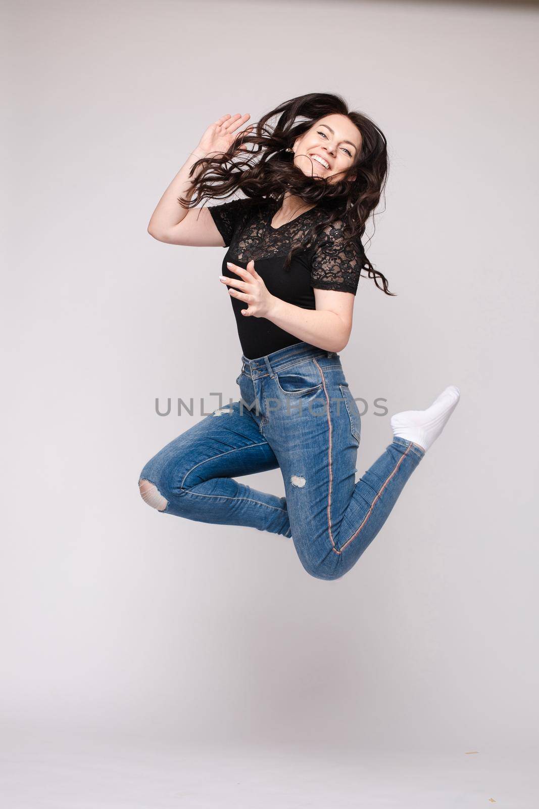 Cheerful brunette young woman in casual outlook jumping in mid air in studio. by StudioLucky