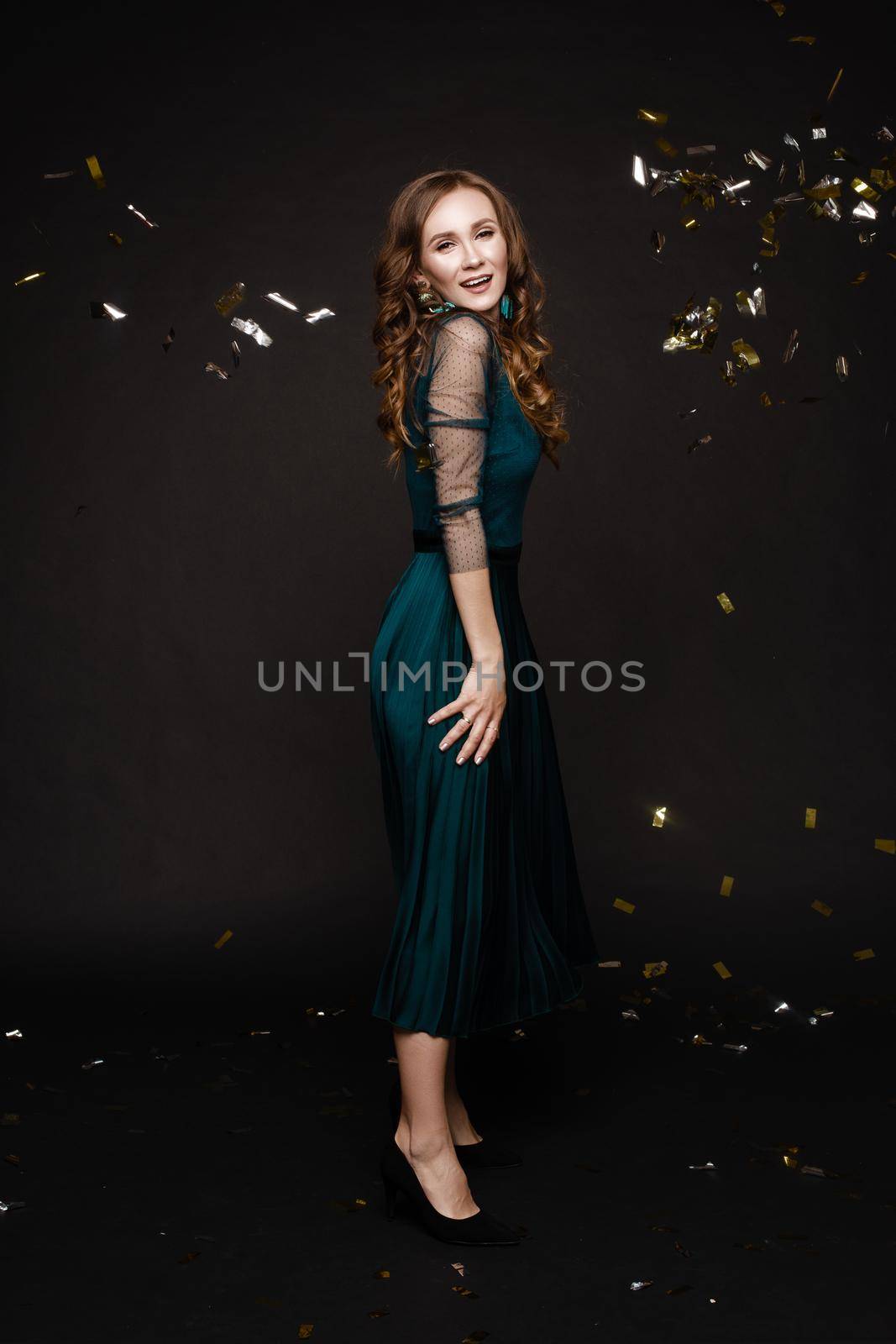 Front view of elegant woman wearing long black dress looking at camera and smiling on black isolated background. Attractive blonde with long legs posing in studio. Concept of party and beauty.