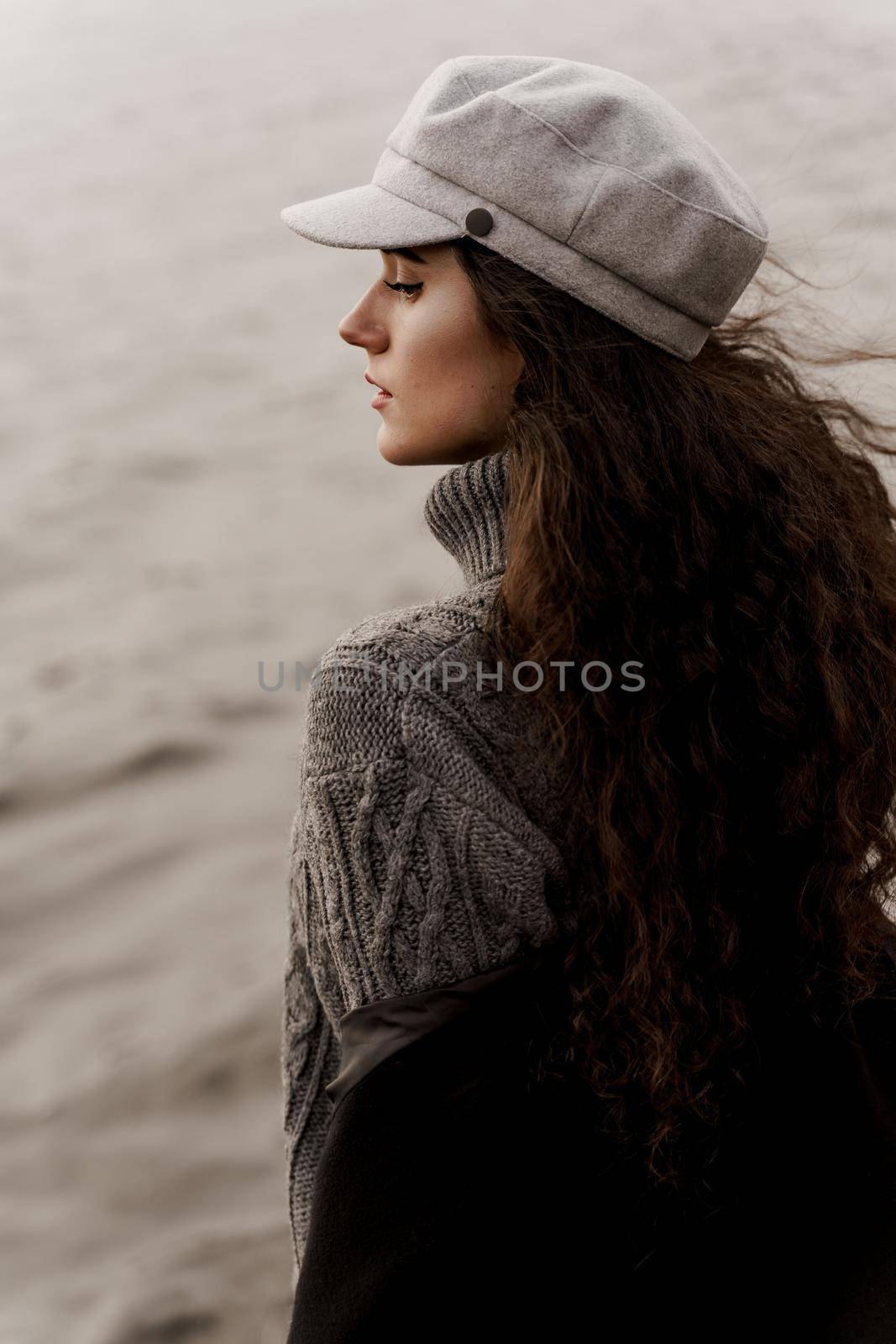 A beautiful girl close-up in a black coat and a gray woolen cap near the lake. Traveling in your country. by Rabizo