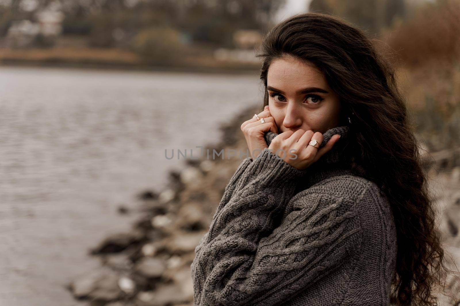 Girl with curly hair on the background of birch with stones and lake in autumn.