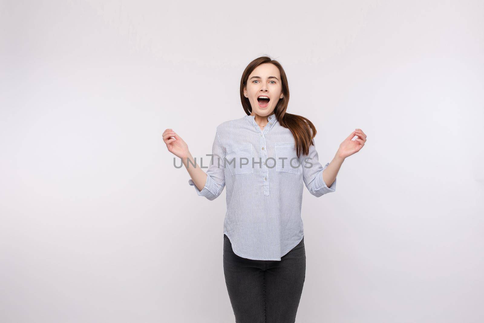 Amazed woman jumping with open mouth.Studio portrait of a young girl with brunette hair wearing casual clothes jumping because of surprise by StudioLucky