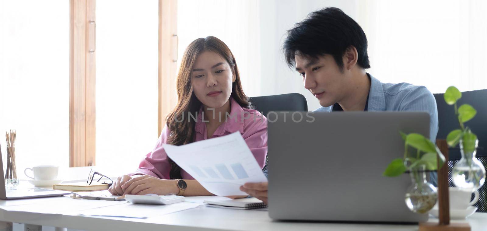 Two Cheerful Asian young business people working together using a tablet at a modern office.doing planning analyzing the financial report, business plan investment, finance analysis concept by wichayada