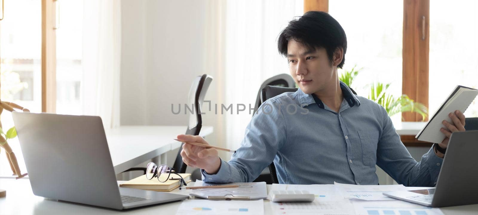 Portrait of Young Asian man hand freelancer is working her job on computer tablet in modern office. Doing accounting analysis report real estate investment data, Financial and tax systems concept. by wichayada