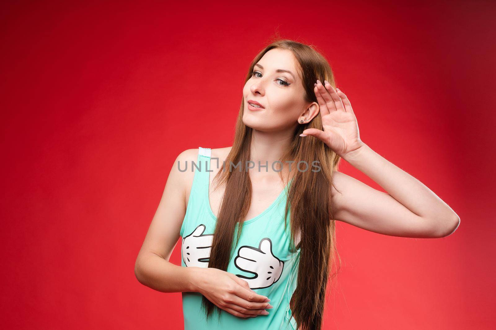 Studio portrait of curious brunette girl in multicolored top listening to the news or gossips with her ear.