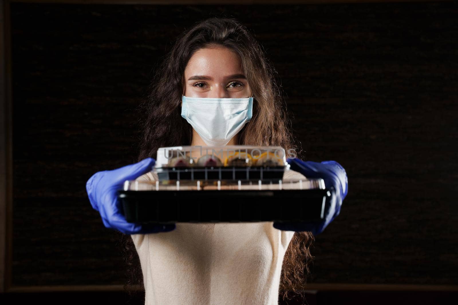 Girl with sushi. Food courier in medical mask. Delivery at quarantine coronavirus covid-19. Young woman holding 2 sushi boxes in hands using gloves