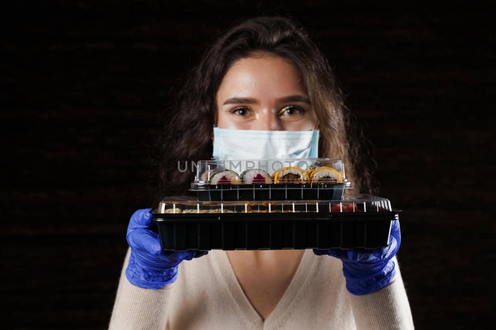 Girl sushi courier in medical mask with 2 boxes. Sushi set in box healthy food delivery service by car. Japanese cuisine: rolls, soy sauce, wasabi.