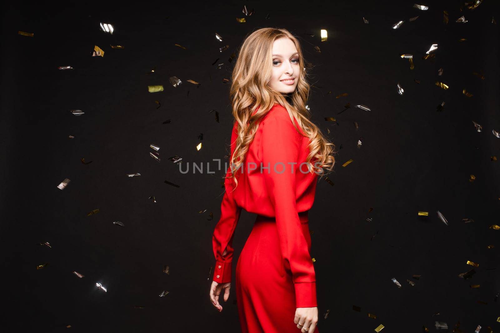 Front view of elegant woman wearing long black dress looking at camera and smiling on black isolated background. Attractive blonde with long legs posing in studio. Concept of party and beauty.