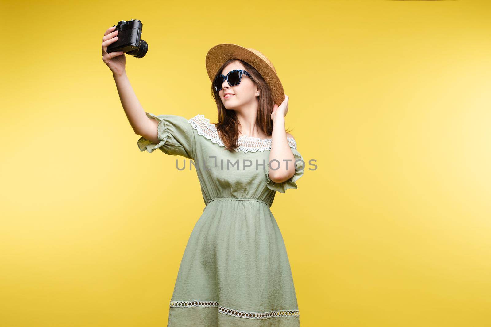 Happy traveler woman posing making selfie using camera isolated at yellow studio background by StudioLucky