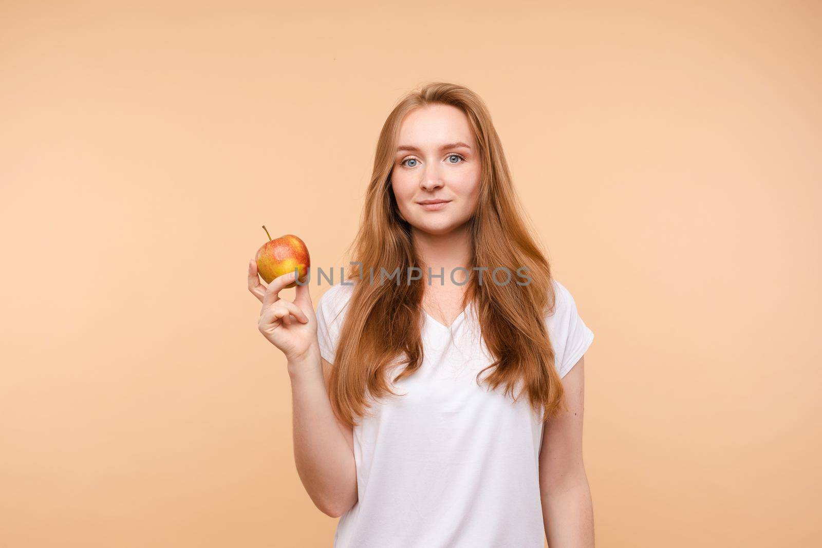 Beautiful young girl with tied on back hair eating tasty apple on lunch. Side view of attractive model promoting healthy lifestyle. Brunette woman with white teeth holding delicious fruit in her hand.