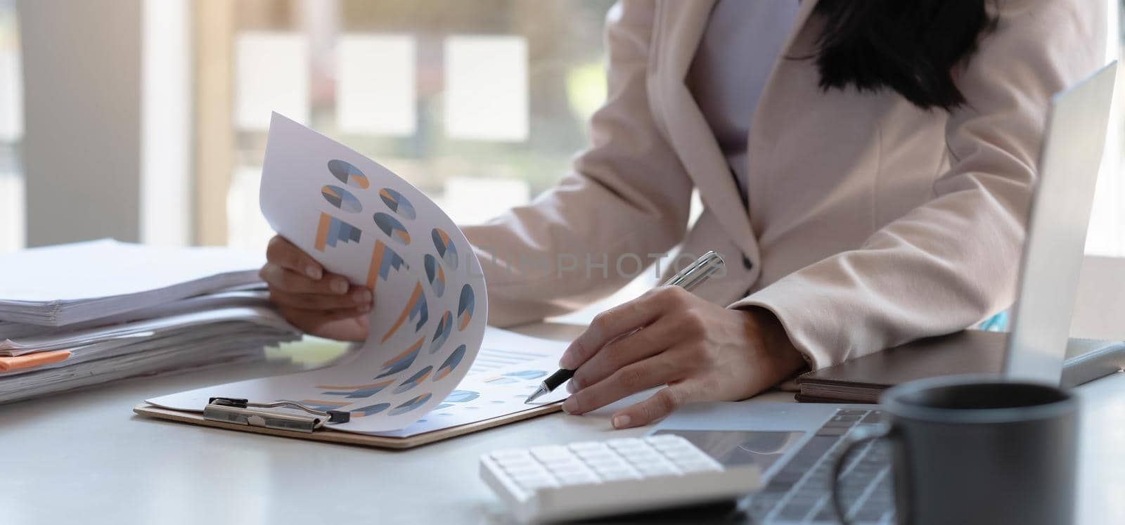 Businesswoman pointing pen at data graph, estimating profit and income statement of business in office..