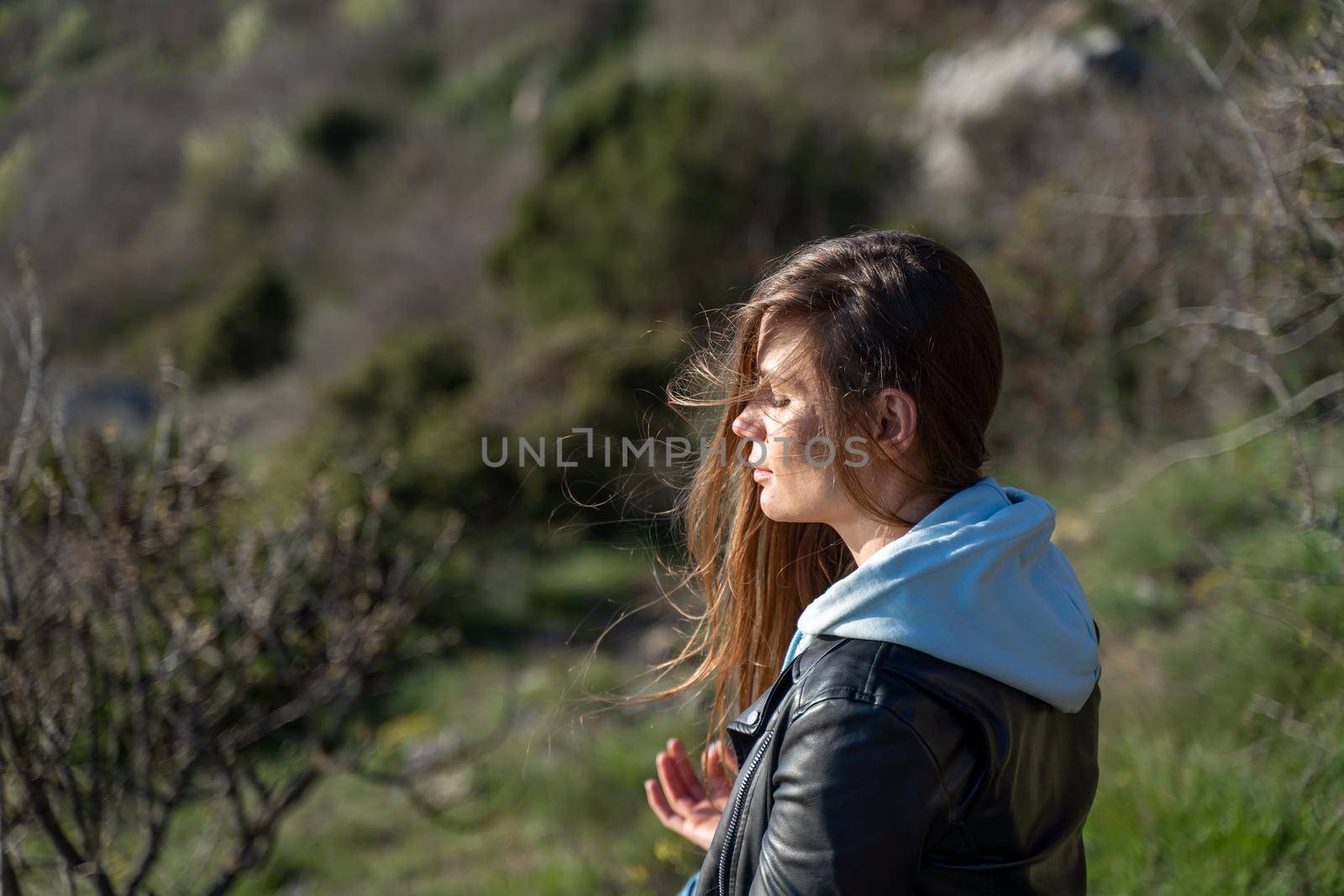 Woman tourist enjoying the sunset over the sea mountain landscape. Sits outdoors on a rock above the sea. She is wearing jeans, a blue hoodie and a black leather jacket. Healthy lifestyle, harmony and meditation.