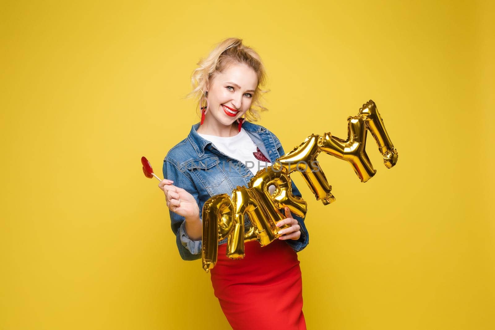 Attractive happy woman laughing holding big gold letters posing at yellow studio background medium long shot. Beautiful fashionable young girl relaxing having positive emotion