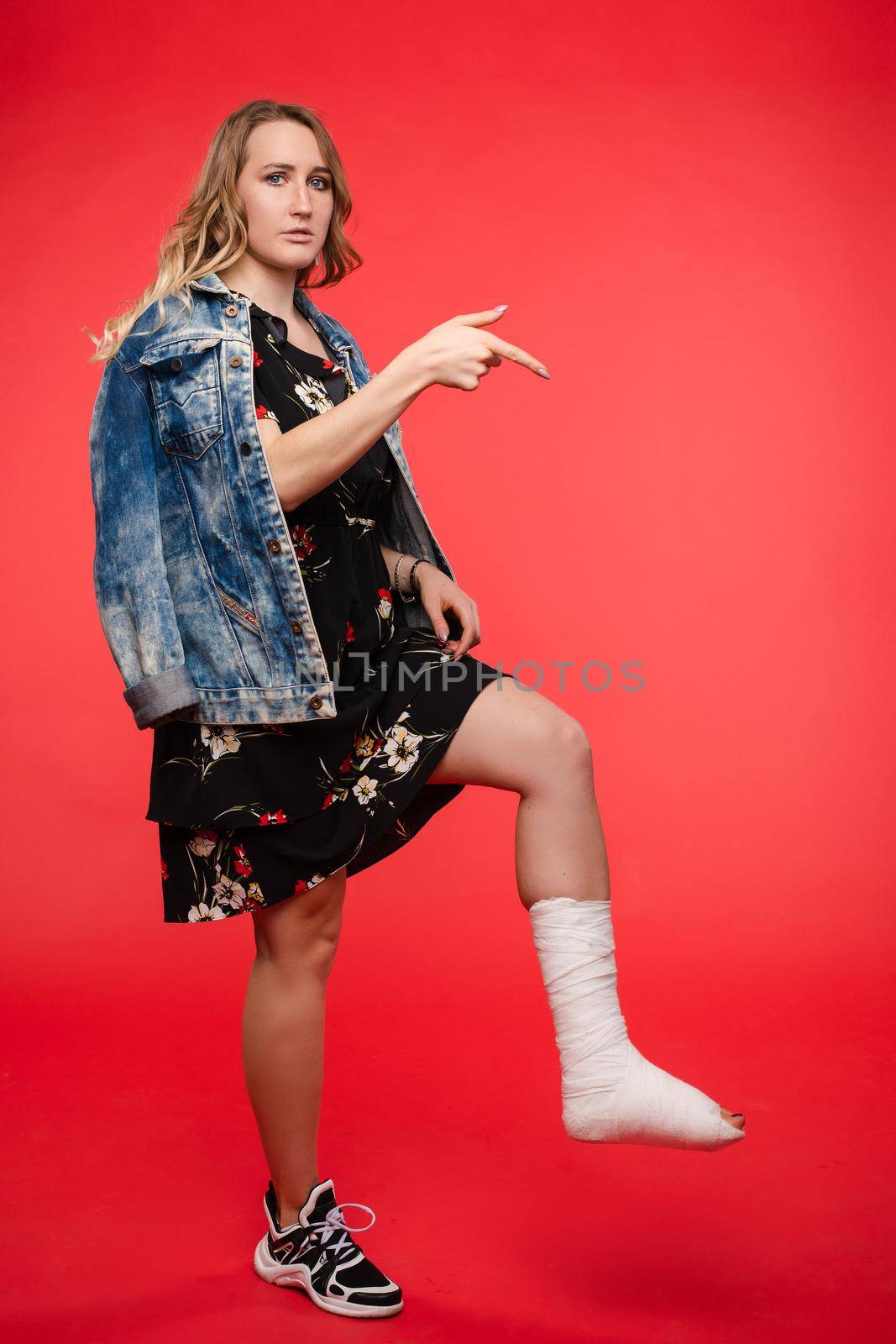 Girl standing on red isolated background with broken leg by StudioLucky