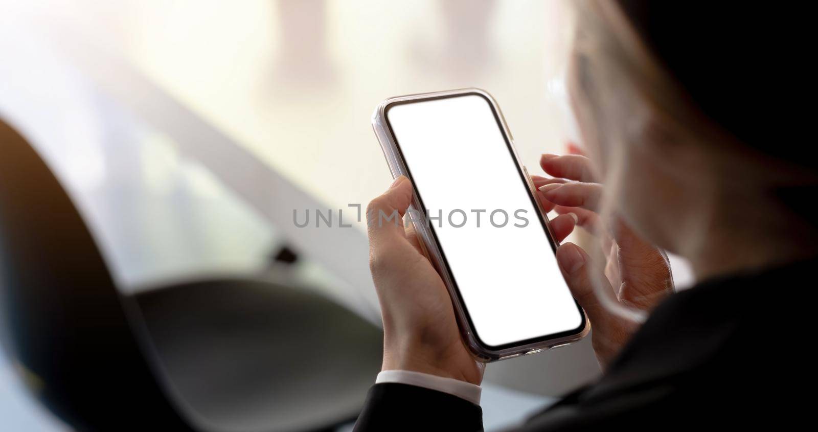 Close-up of a woman hand holding a smartphone white screen is blank the background is blurred.Mockup..