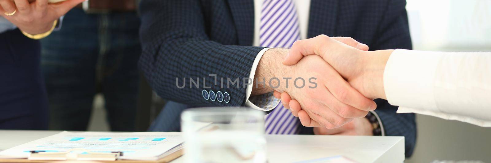 Focus on business male performing friendly gesture towards colleague. Smart man in classy suit shaking hands with young manager. Company meeting concept. Blurred background