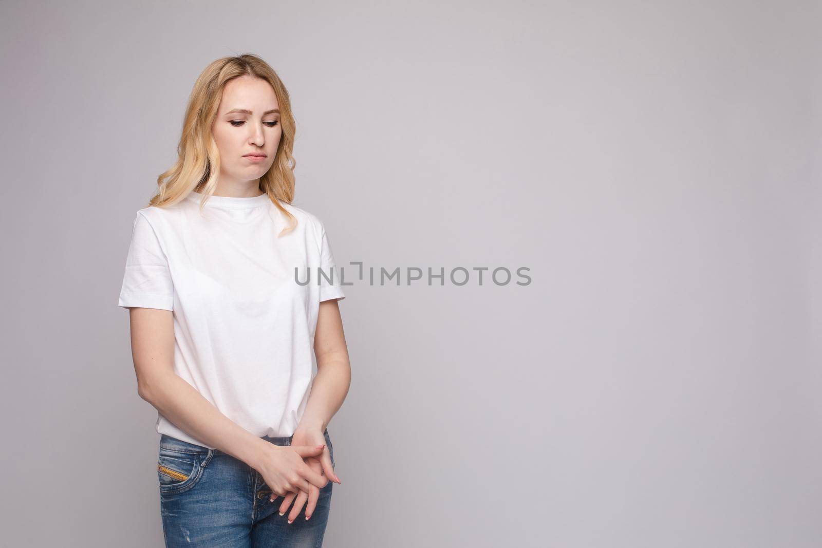 Upset young beautiful woman standing with crossed hands isolated at white studio background medium long shot. Unhappy European female looking down having negative emotion