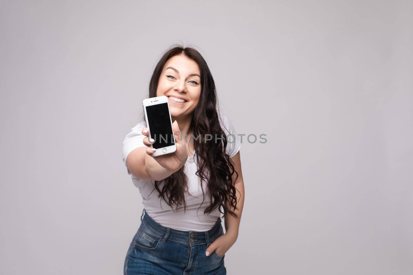 Pretty girl pointing at cell phone.Studio portrait of beautiful caucasian by StudioLucky