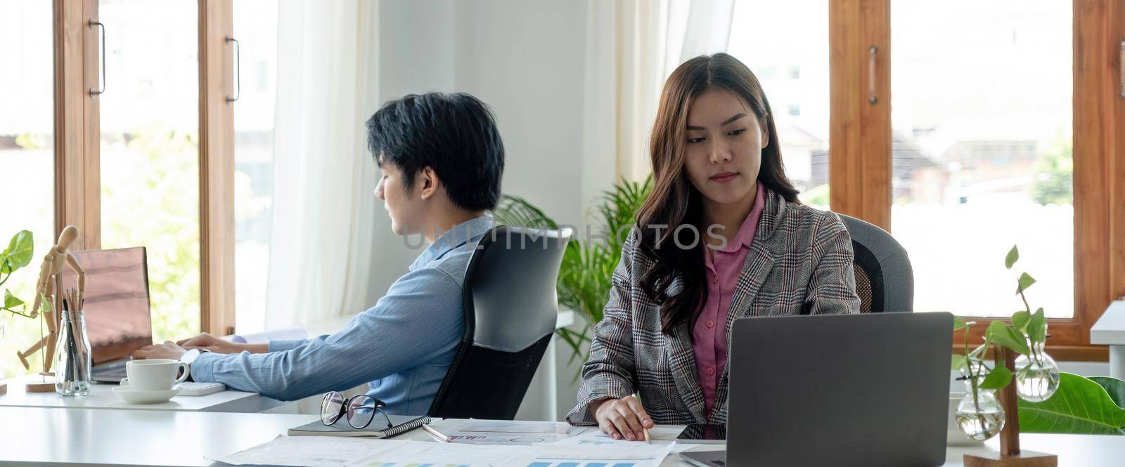 Portrait of young asian woman sitting at her desk with laptop while looking at laptop in modern office. by wichayada
