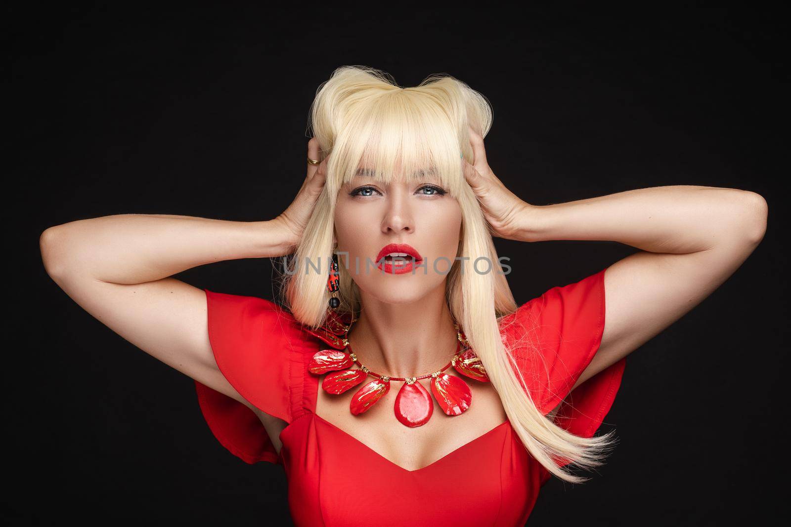 Stock headshot of sexy blonde woman with red lips in red dress and red accessories holding arms in her hair. She is opening her mouth slightly.