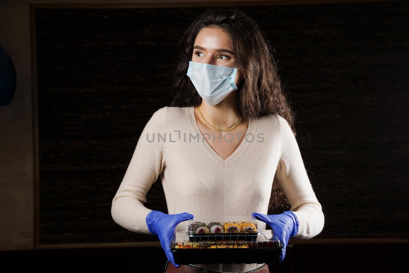 Girl with sushi. Food courier in medical mask. Delivery at quarantine coronavirus covid-19. Young woman holding 2 sushi boxes in hands using gloves