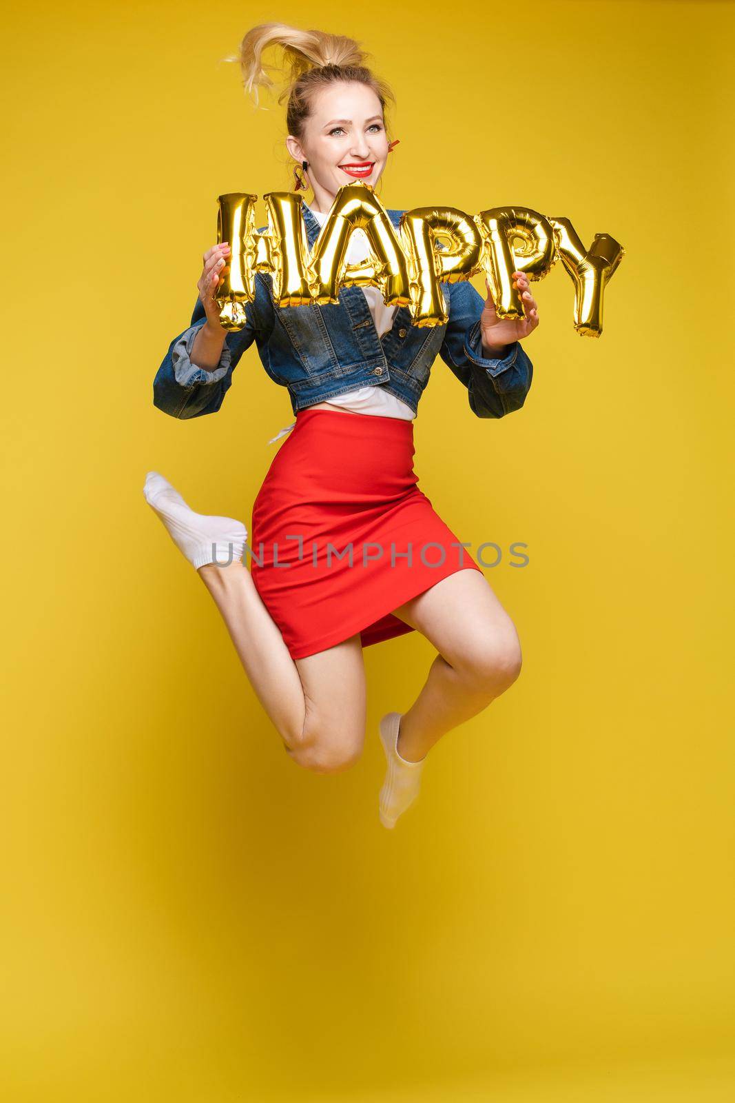 Full length isolate portrait of positive brunette young girl in jeans and t-shirt and sneakers jumping over yellow background. She is smiling at camera.