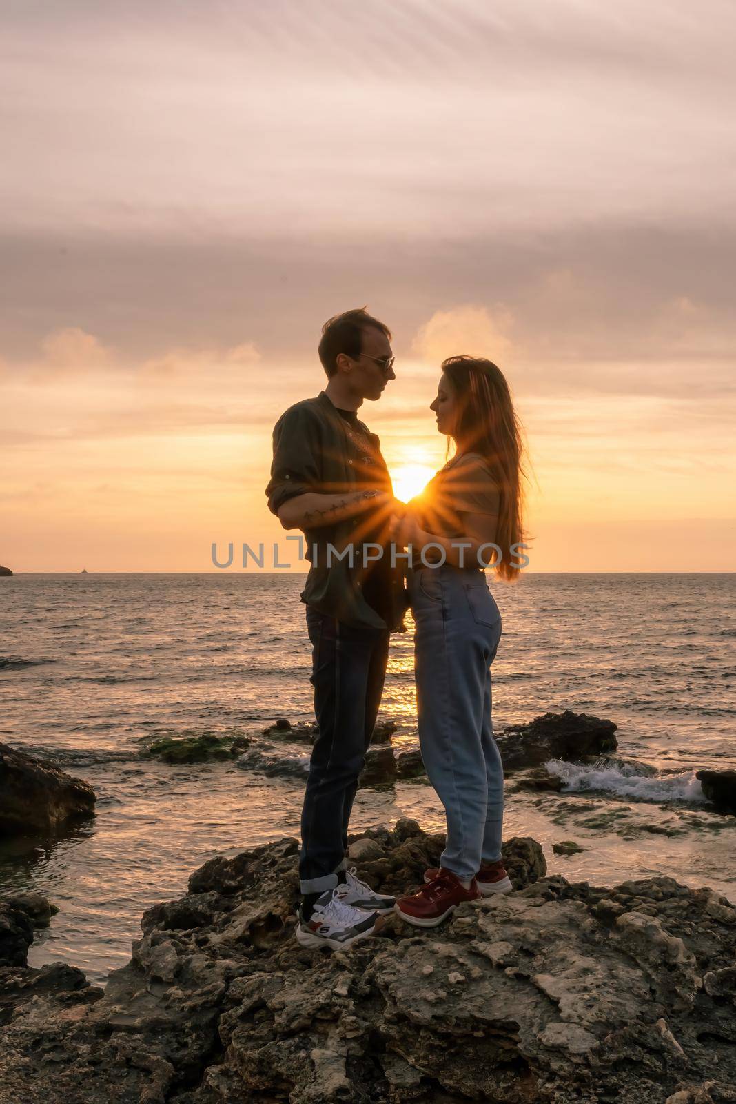 silhouettes in love romantic couple lovers hugging, kissing, touching, eye contact at sunset, sunrise on the background of the sea, the sun, the clouds in fiery red, orange colors by Matiunina