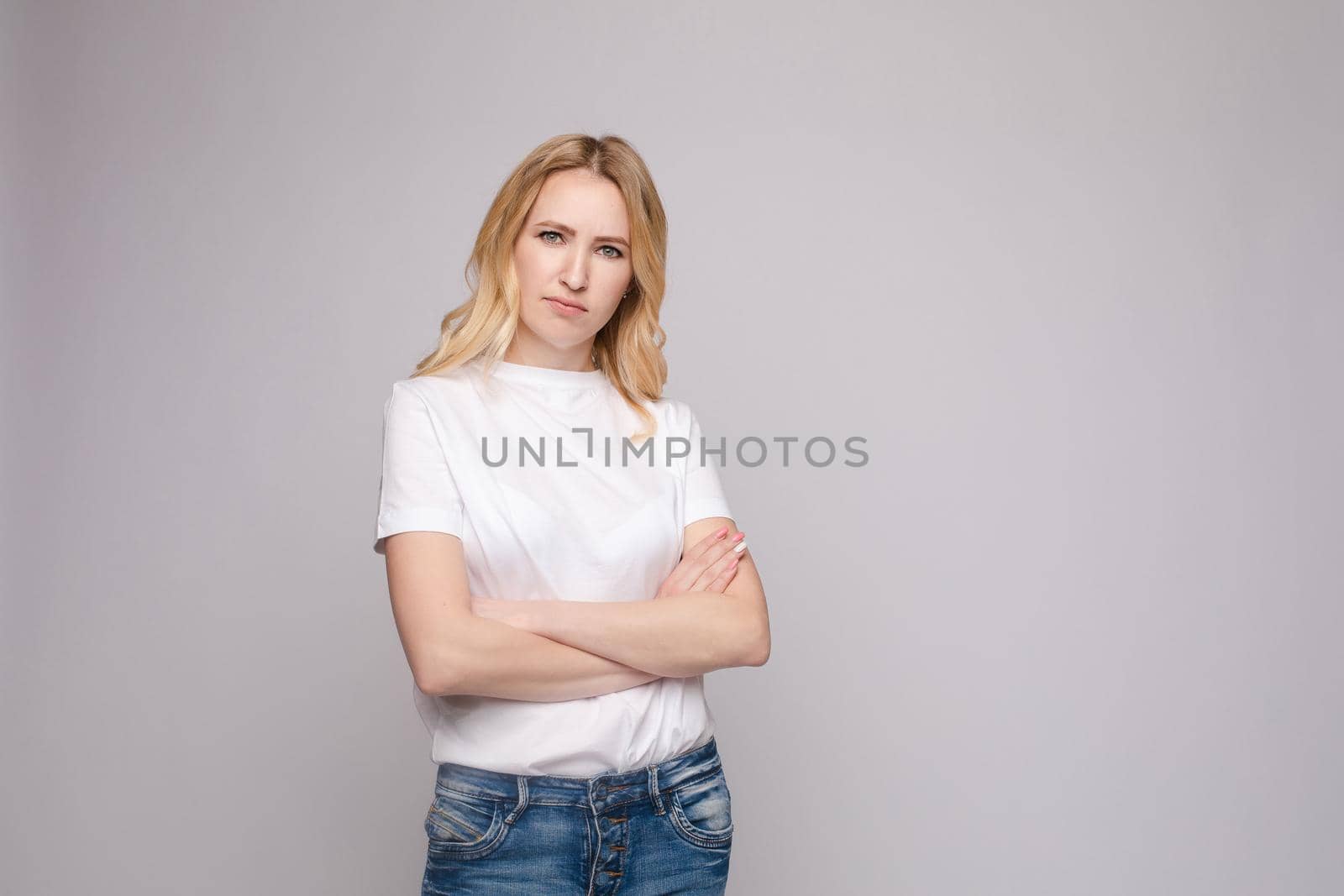 Studio portrait of unsatisfied young brunette caucasian woman with wavy hair in overall with colorful pattern holding arms folded and looking at camera with grief, dissatisfaction, anger and disbelief. Isolate.