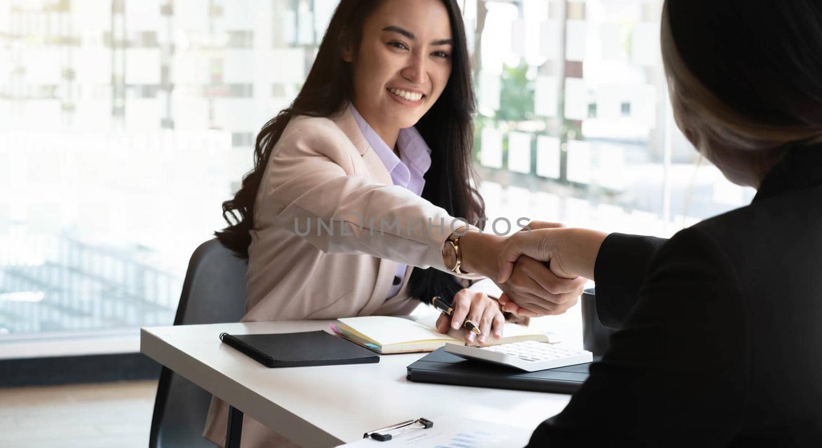Smiling Young Asian businesswoman shaking hands happy meeting negotiations success with graph papers placed at the office. by wichayada