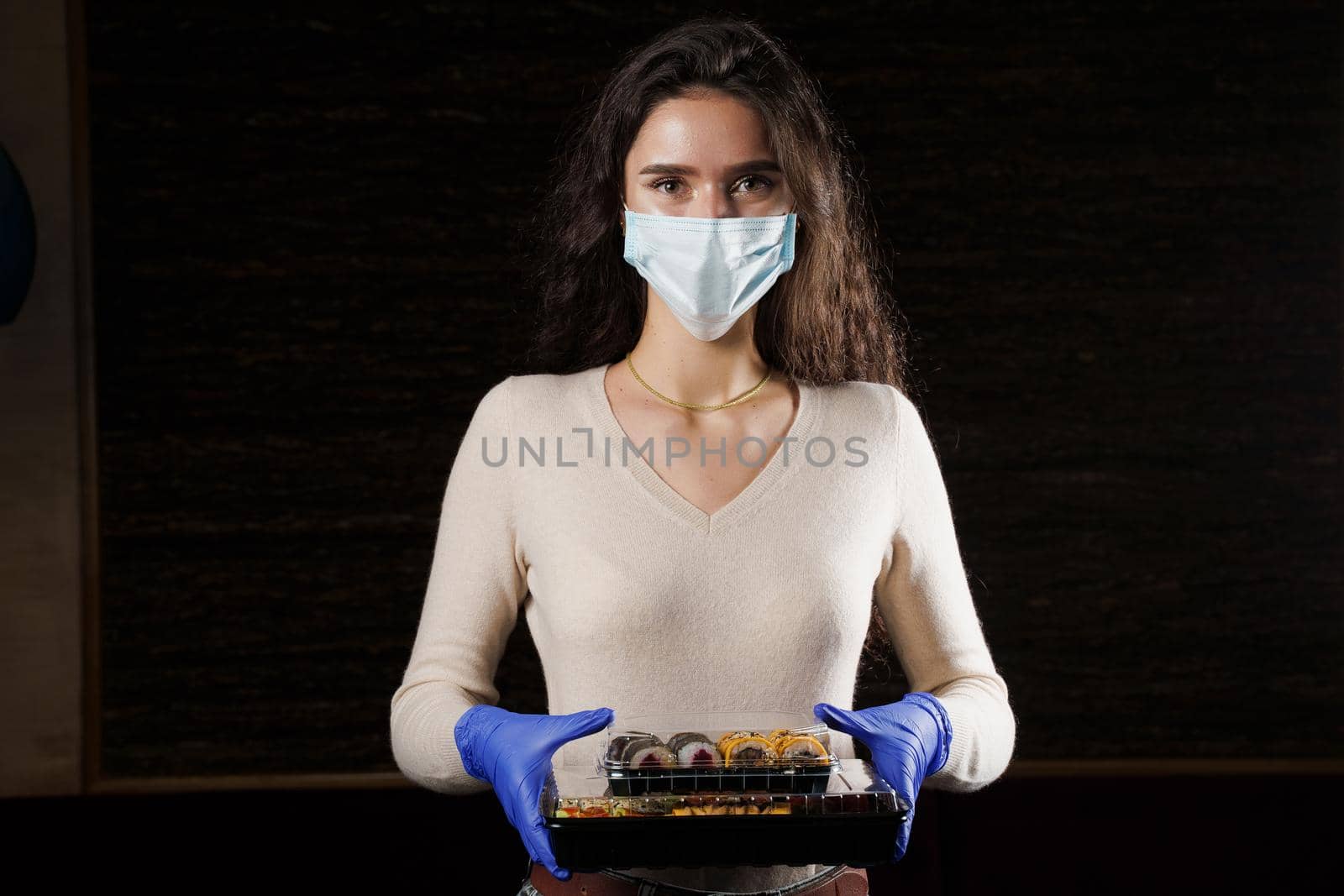 Girl with sushi. Food courier in medical mask. Delivery at quarantine coronavirus covid-19. Young woman holding 2 sushi boxes in hands using gloves