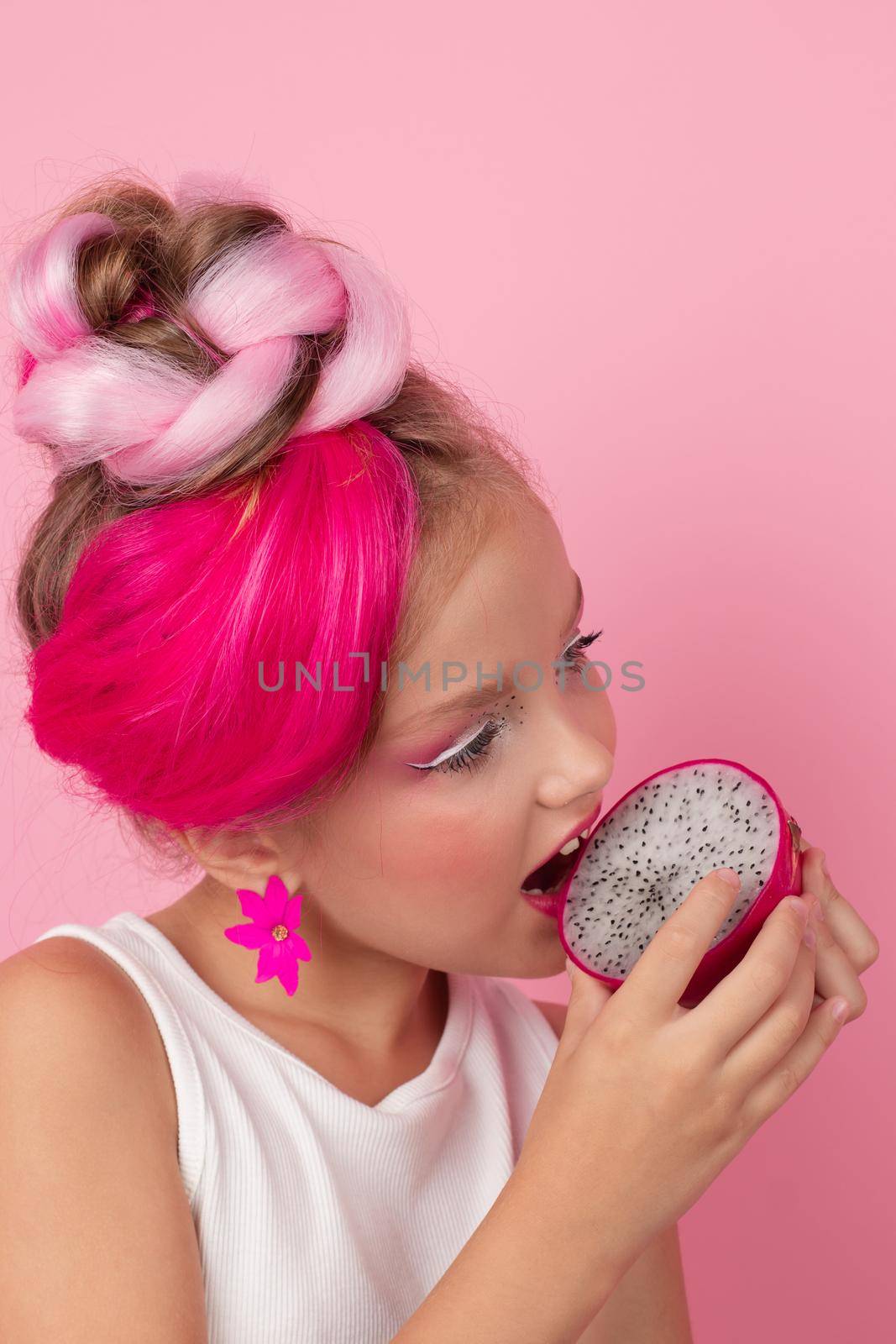 Close-up portrait of pretty girl with pink hairstyle with dragon fruit on pink background. Studio shot of charming tween girl with pink make up enjoying juicy red pitaya. exotic Pitahaya fruit by oliavesna