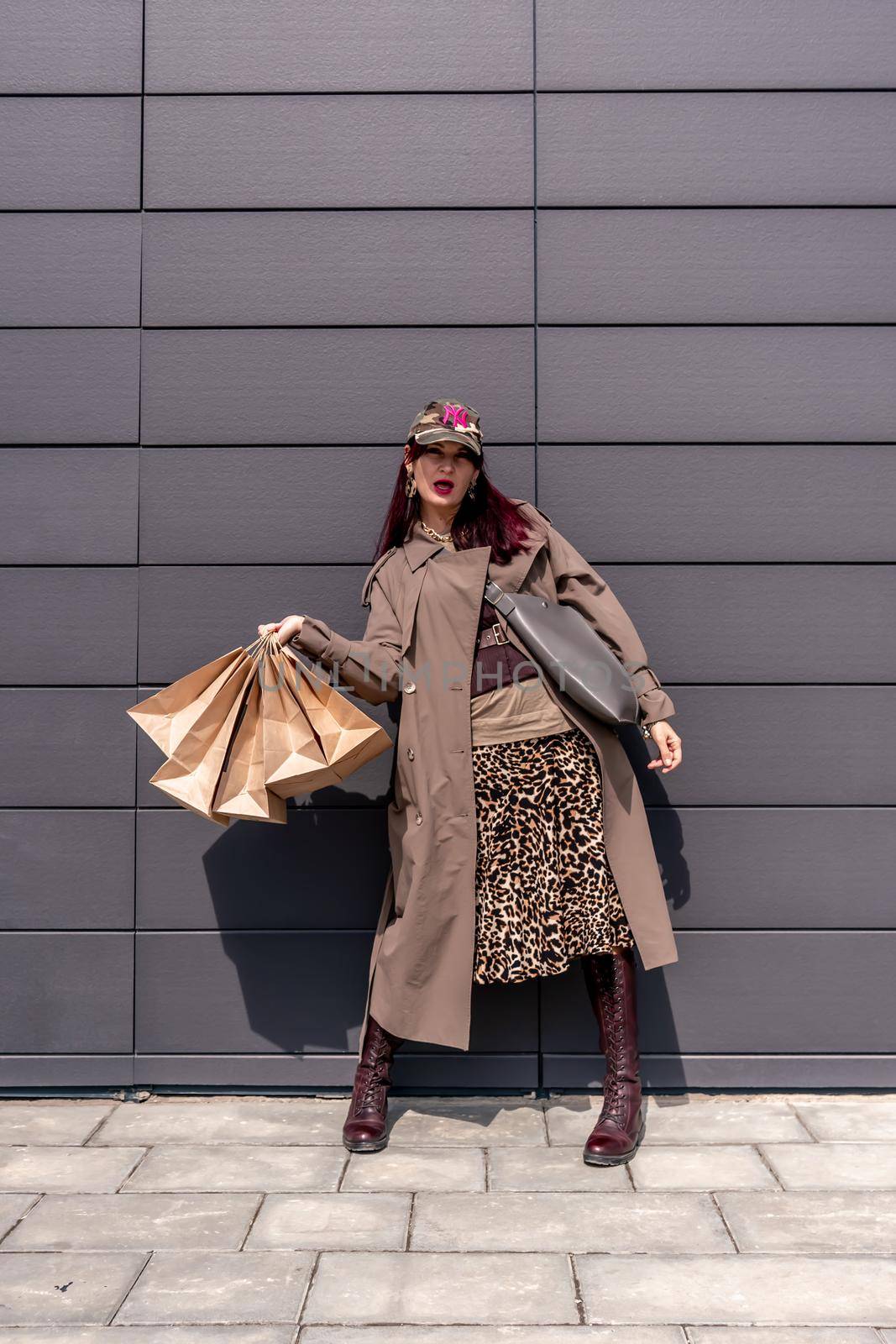 A happy shopaholic girl keeps her bags near the shopping center. A woman near the store is happy with her purchases, holding bags. Dressed in a leopard print dress. Consumer concept