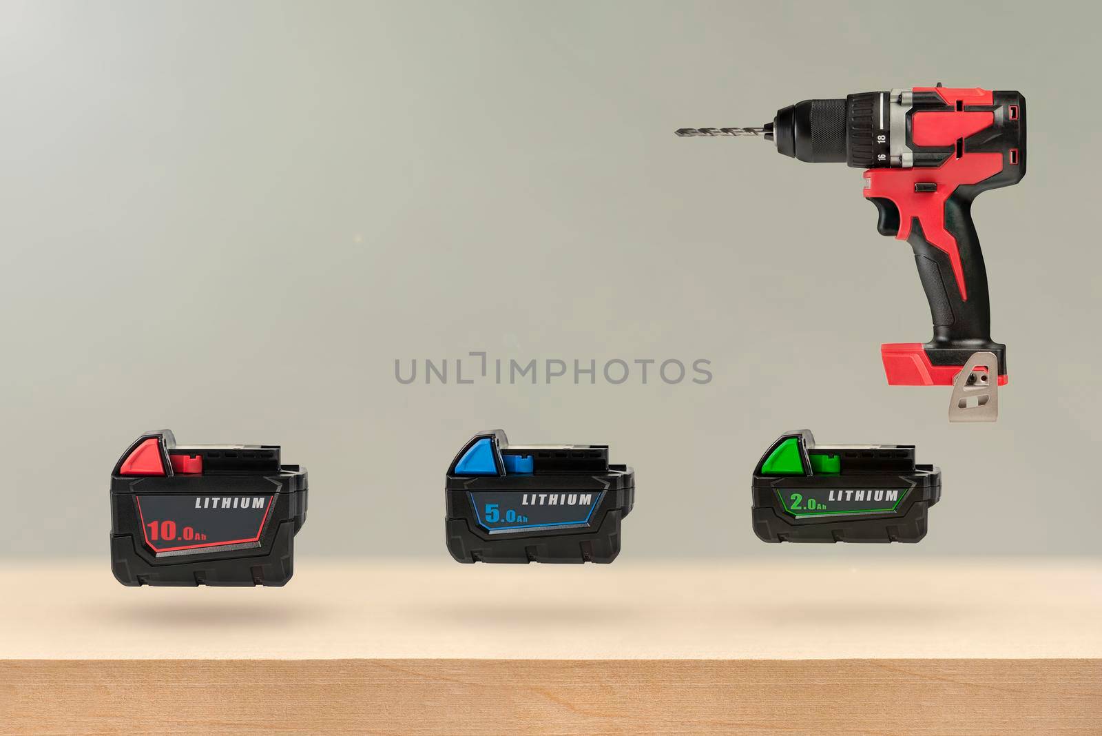 Batteries for cordless tools. Batteries for a screwdriver of different capacities and different sizes. Electric drill and three batteries with a charge indicator on a wooden background by SERSOL