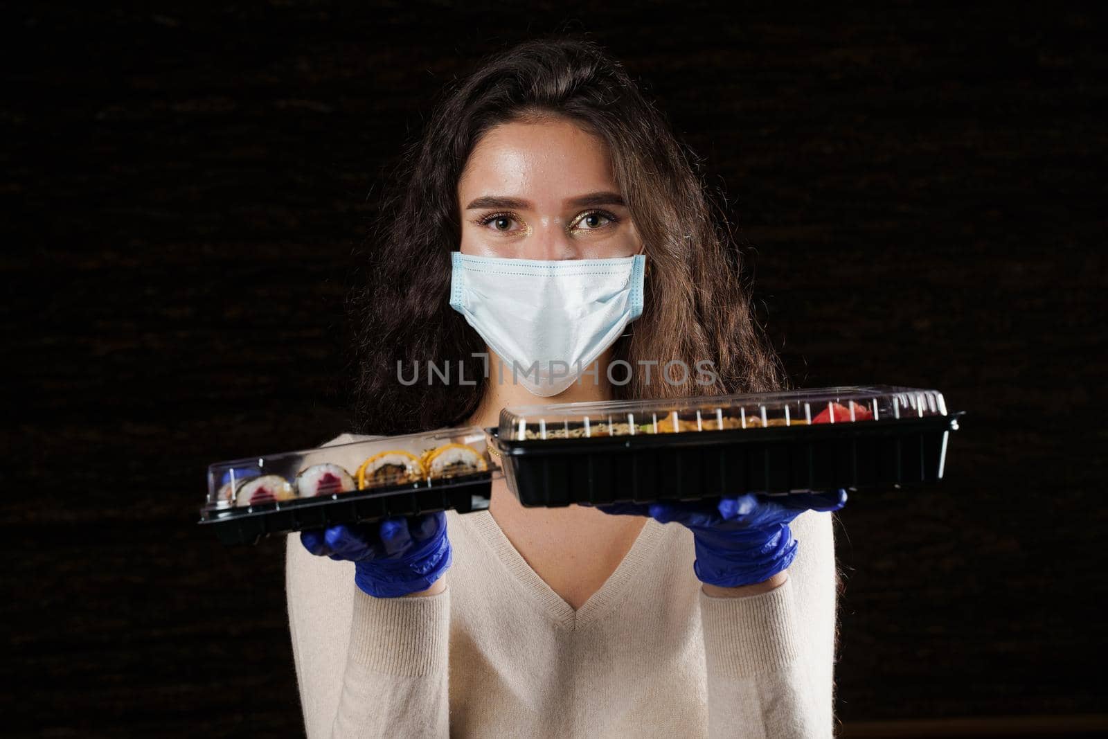 Girl sushi courier in medical mask with 2 boxes. Sushi set in box healthy food delivery service by car. Japanese cuisine: rolls, soy sauce, wasabi.