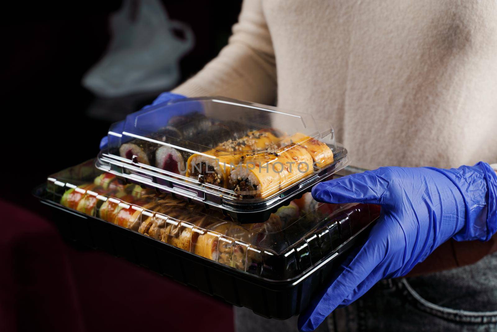 Sushi roll food delivery service at quarantine covid-19 period. Holding sushi set box using medical gloves on black background